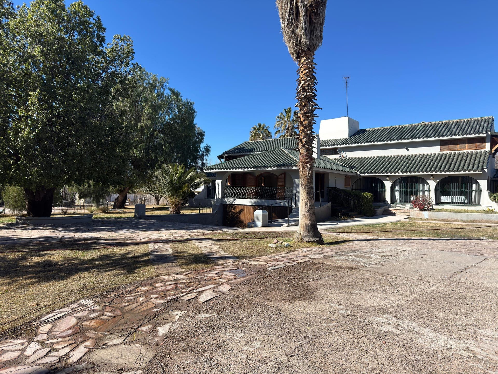 Fachada de la residencia LAM Chacras Larrea con su parque y palmeras en Chacras de Coria